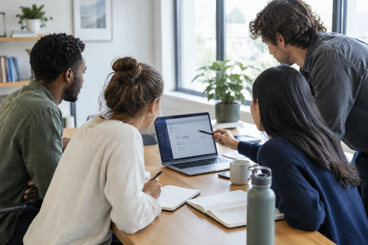 Deux collègues examinent ensemble un outil numérique sur un ordinateur portable, avec des notes posées sur la table.