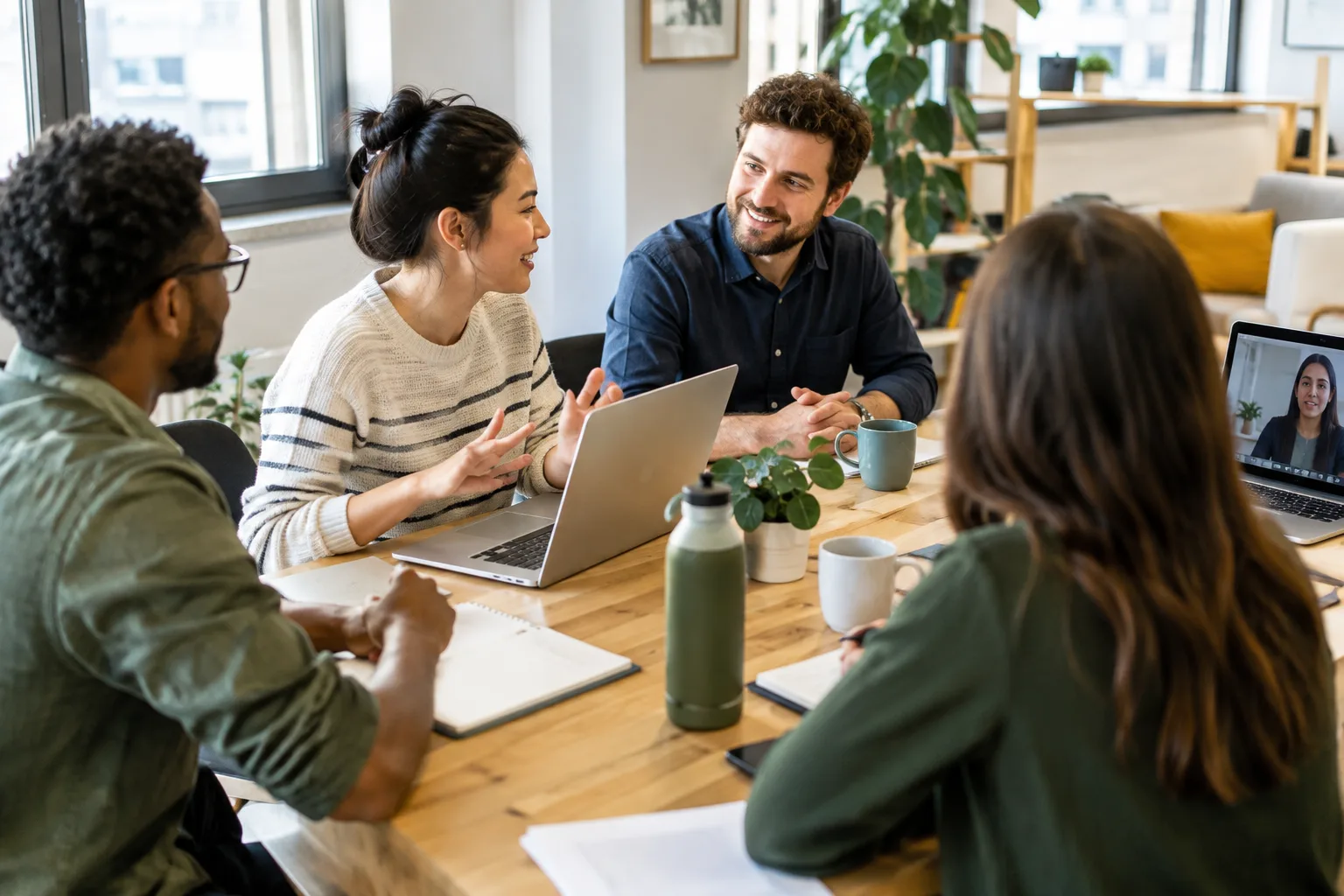 Des collègues réunis autour d’une table échangent tandis qu’une personne participe à distance.
